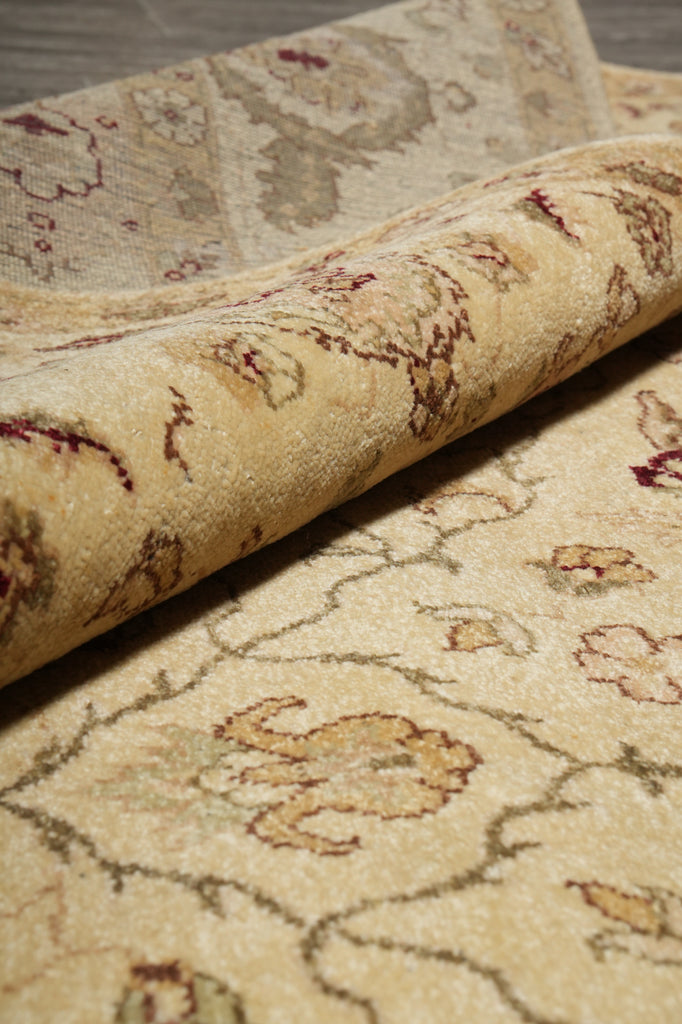 A close-up of a rolled area rug showing its cream and beige base with traditional floral motifs in muted burgundy, olive green, and tan.