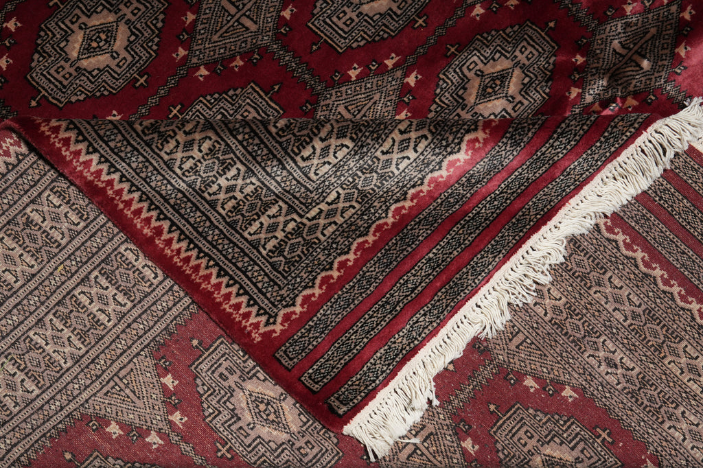 A close-up of a patterned rug with deep red, black, beige, and white geometric motifs and white fringe.