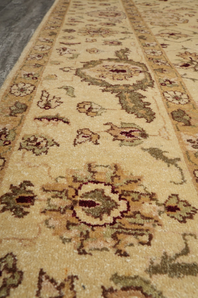 A close-up view of a traditional patterned area rug with a warm beige base, featuring floral motifs and ornate medallions in muted brown, olive green, and cream tones.