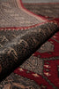 Load image into Gallery viewer, Close-up of a patterned rug with a folded section showing a deep red field, beige and black geometric motifs, and a dark central border.