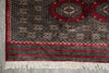 Load image into Gallery viewer, A close-up of a traditional patterned rug corner showing a red field, black and beige geometric motifs, decorative borders, and white fringe at the bottom.