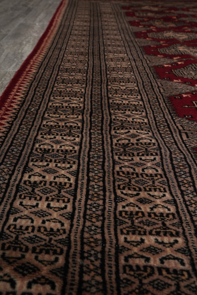 A close-up of a patterned rug with horizontal bands of black, beige, and red geometric motifs.
