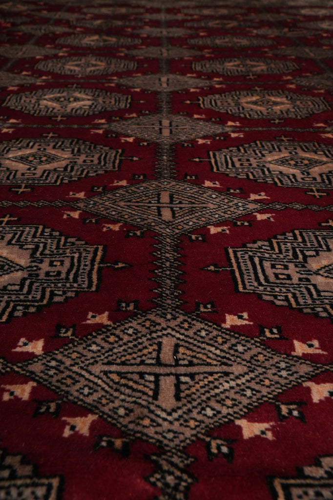 A close-up view of a traditional patterned rug with a deep red field, beige and black geometric medallions, and small cream accents.