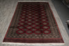 Load image into Gallery viewer, A rectangular area rug with a traditional geometric pattern in deep red, dark brown, and beige, featuring white fringe on the bottom, laid out on a gray wood-look floor.