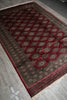 Load image into Gallery viewer, A traditional oriental area rug with a dark brown and red geometric pattern, laid out diagonally on a gray tiled floor.