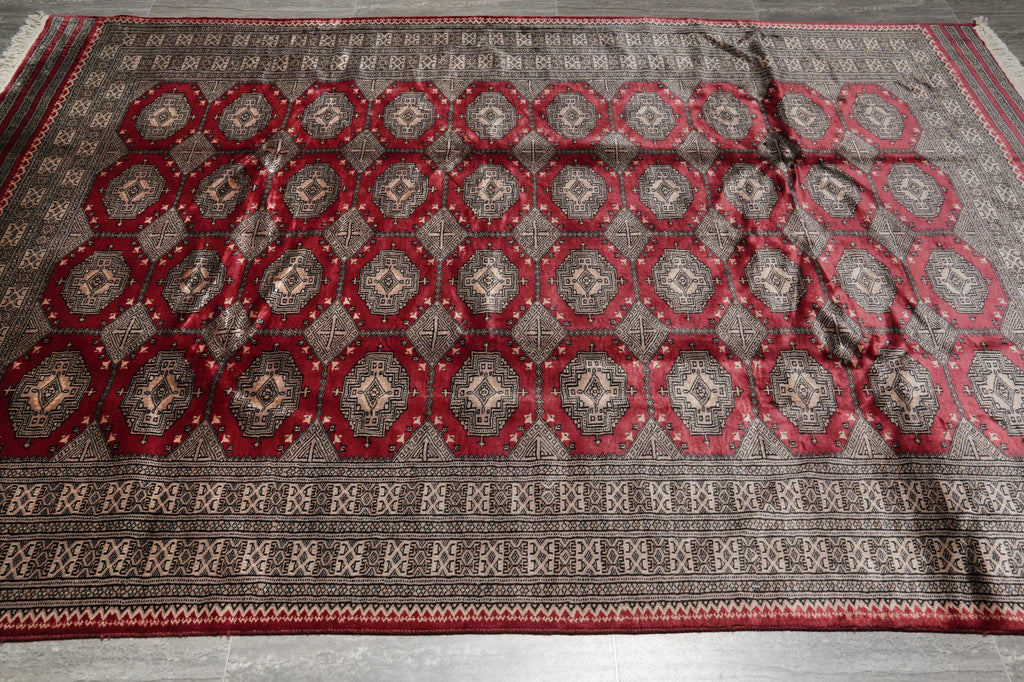 A large traditional area rug with a dark gray and red geometric pattern, laid flat on a gray floor.