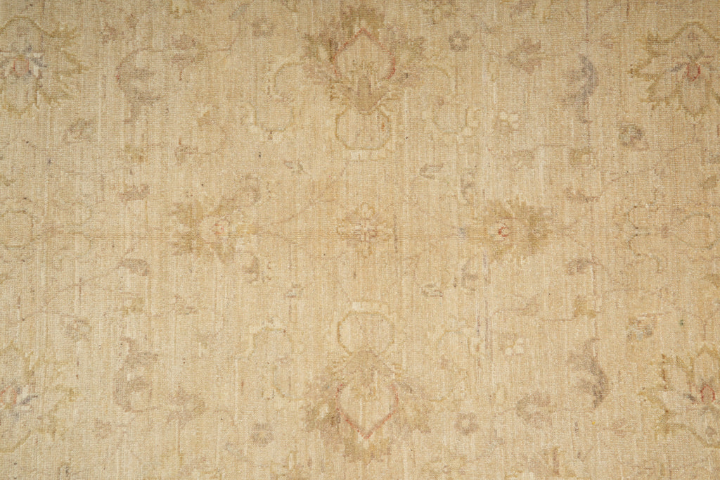 A close-up of a beige fabric or wallpaper pattern with a subtle, faded floral and medallion design in tan, light brown, and soft pink tones.