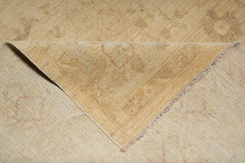 A close-up of a folded beige area rug showing its woven texture and subtle distressed floral patterns.