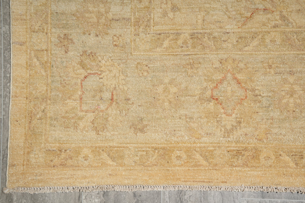 A close-up of a vintage-style area rug with a distressed beige and tan base, featuring faded red diamond medallions and traditional geometric borders, laid out on a gray tiled floor.