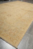 Load image into Gallery viewer, A large beige area rug with a faded traditional floral pattern and fringed edges, shown laid out on a gray tiled floor.