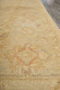 Load image into Gallery viewer, A close-up view of a beige area rug with a faded traditional pattern and a subtle dusty red diamond motif, laid out on a gray floor.