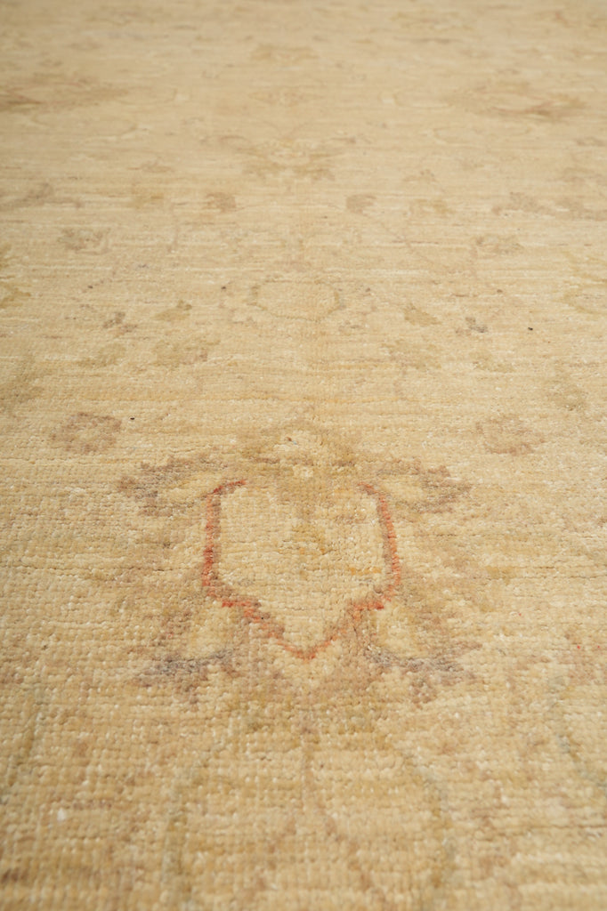 A close-up view of a light beige area rug with a faded, distressed traditional pattern in muted rust red and gray tones.