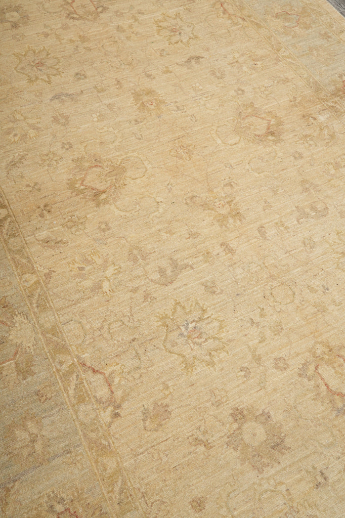 A close-up of a beige area rug with a faded, distressed floral and scroll pattern in muted tan and brown tones.