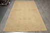Load image into Gallery viewer, A large rectangular area rug in a warm sandy beige color with a faded traditional floral pattern, laid out on a gray wood-look floor.