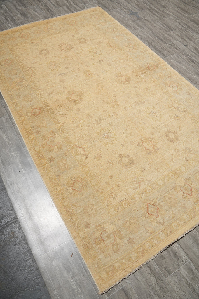 A rectangular area rug with a traditional floral pattern in shades of beige and light brown, shown laid out on a gray wood-look floor.