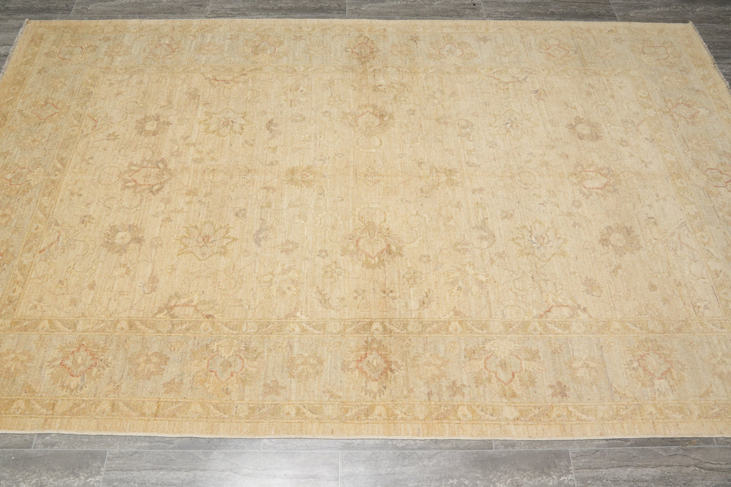 A large rectangular area rug with an intricate traditional floral pattern in shades of beige, tan, and light brown, laid out on a gray tiled floor.