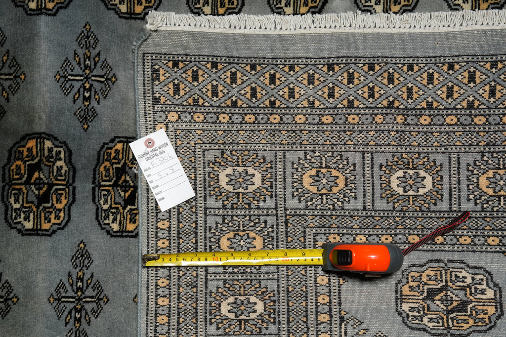 A patterned area rug in gray, black, and beige tones is shown with a yellow tape measure and a product tag laid out on top to indicate size and details.