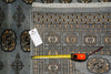 Load image into Gallery viewer, A patterned area rug in gray, black, and beige tones is shown with a yellow tape measure and a product tag laid out on top to indicate size and details.