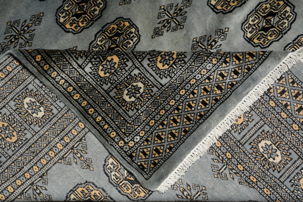 A close-up of a patterned area rug with a light gray base, black and gold geometric borders, and white fringe on one corner.