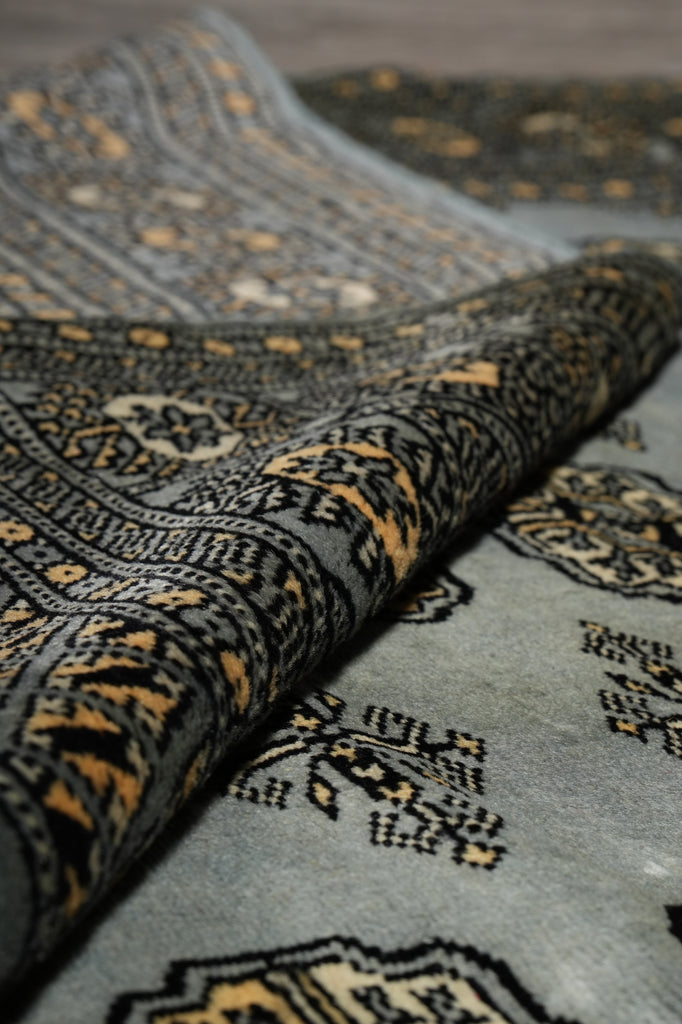 Close-up of a folded area rug showing its detailed woven pattern in charcoal gray, black, and ochre gold.