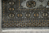 Load image into Gallery viewer, A close-up of a patterned area rug showing its corner, detailed medallion motifs, geometric borders, and white fringe tassels on a gray background.