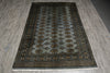Load image into Gallery viewer, A rectangular area rug with a dark gray and black base, featuring a central field of repeating gold and brown medallions and ornate borders, laid out on a gray wood-look floor.