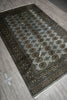 Load image into Gallery viewer, A rectangular area rug with a gray-blue field, black border, and repeating gold and brown medallion motifs, shown laid out on a gray wood-look floor.