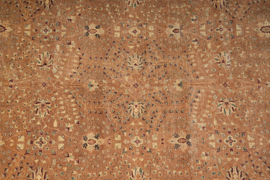 A close-up of a traditional patterned rug in warm tan and brown tones with repeating floral and geometric motifs in beige, muted blue, and small red accents.