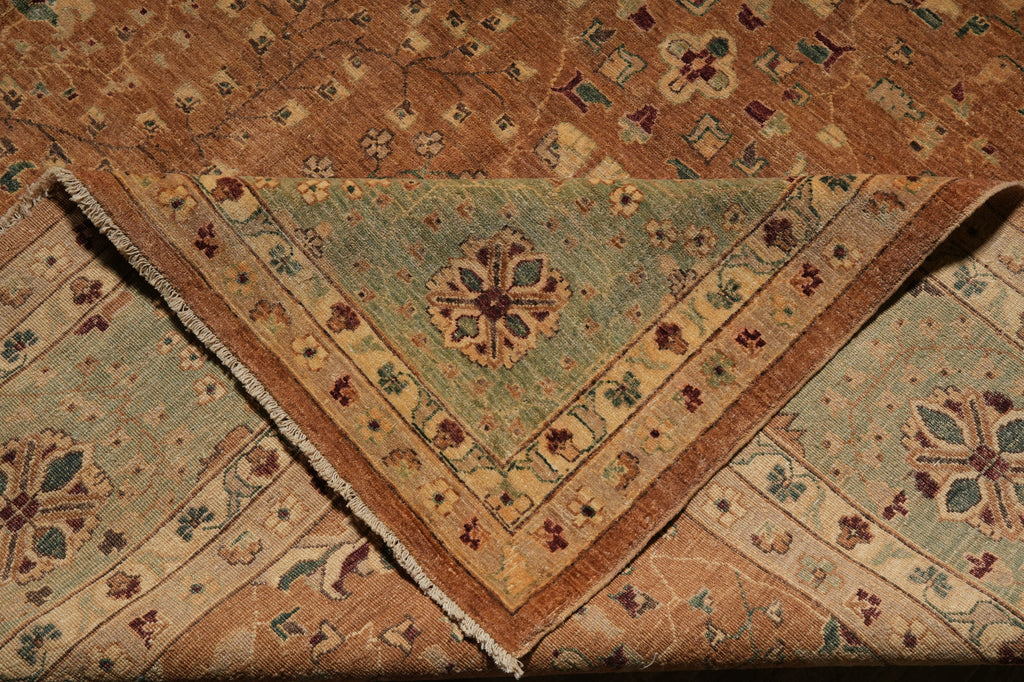 A close-up of a folded vintage area rug showing two patterned sections: a central triangular section in muted sage green with a floral medallion and fringe, surrounded by a warm brown and beige patterned border.