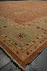 Load image into Gallery viewer, A traditional oriental area rug with a warm brown field, a muted sage green border, and cream fringe, shown laid out on a dark gray floor.
