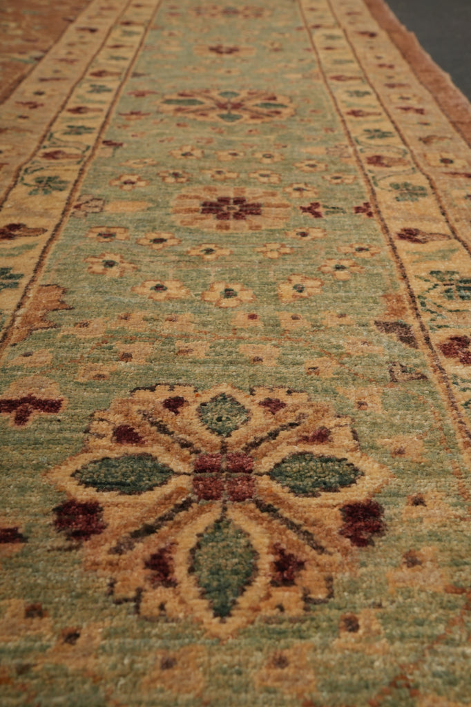 A close-up view of a traditional patterned area rug with a muted sage green center, beige borders, and floral motifs in rust red, olive green, and tan.