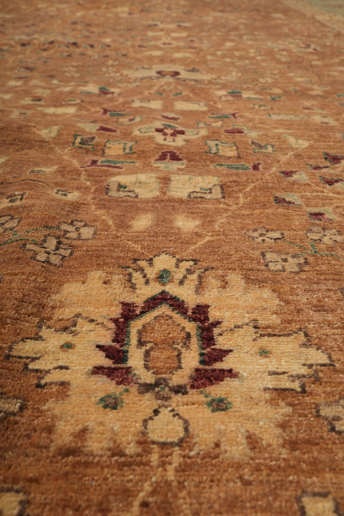 A close-up view of a traditional patterned area rug with a warm brown and beige base, featuring central medallions and floral motifs in rust red, cream, and muted green.