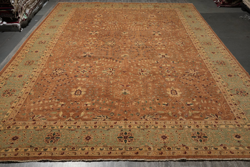 A large traditional oriental area rug with a warm rust-orange center field, detailed floral motifs, and a muted sage-green border, photographed from an overhead angle.