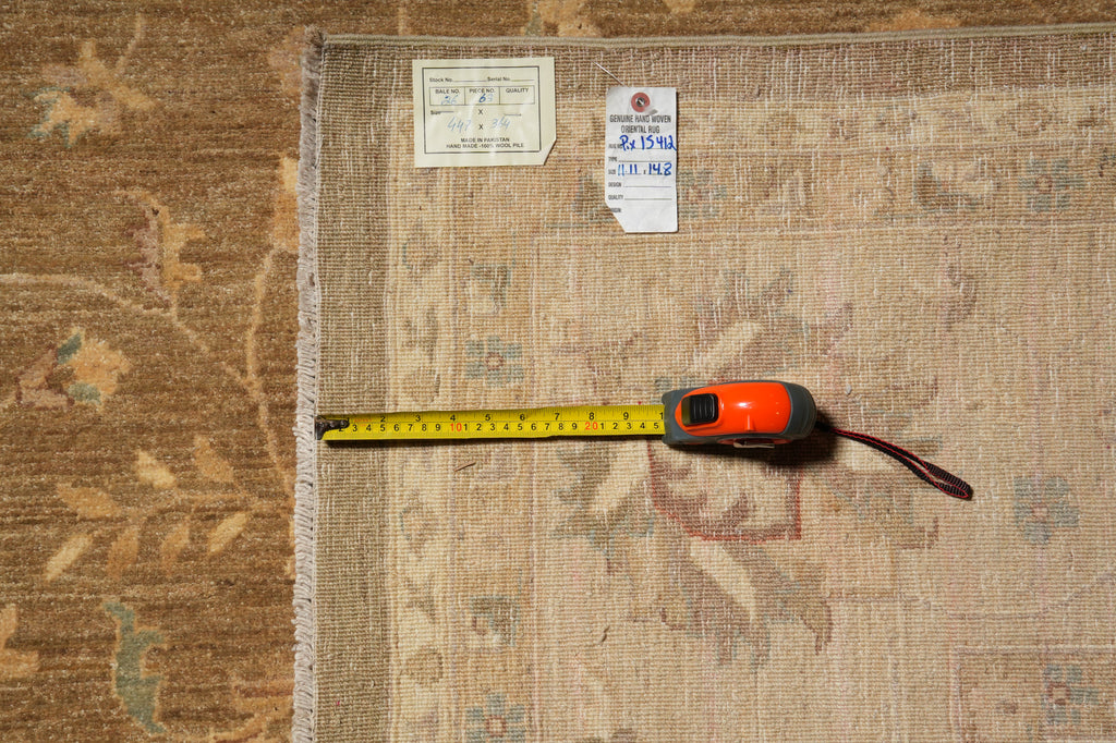 A square area rug laid flat on a matching patterned floor, with a yellow tape measure extended along one edge and two small tags near the top corner.