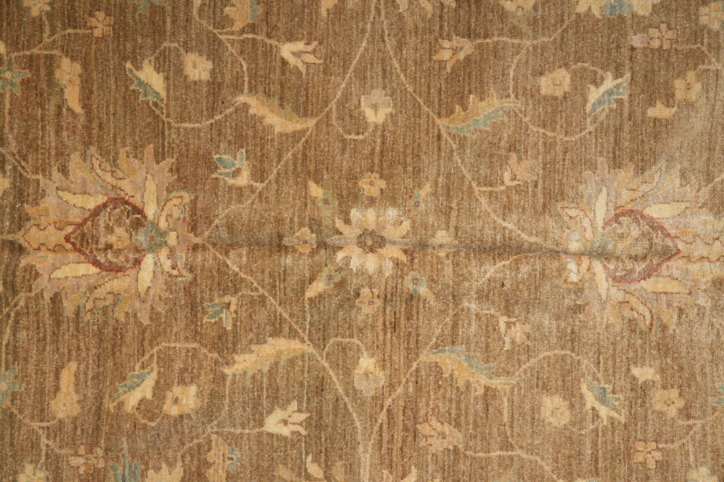 A close-up of a vintage-style floral rug with a distressed, weathered texture. The design features muted beige and tan floral motifs with subtle hints of light blue and reddish-brown accents on a warm brown background.