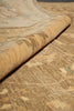 Load image into Gallery viewer, A close-up of a rolled section of a vintage-style area rug showing its textured pile and detailed floral pattern in warm beige, tan, and muted brown tones.