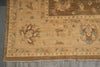Load image into Gallery viewer, A close-up of a traditional oriental rug showing its corner detail, featuring a beige and brown base with floral motifs and small blue accents, laid out on a gray tiled floor.