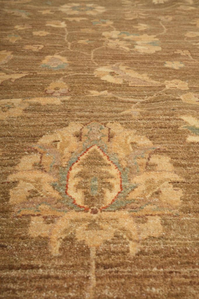 A close-up of a traditional patterned rug with a central floral medallion in beige, brown, and muted blue-green tones.