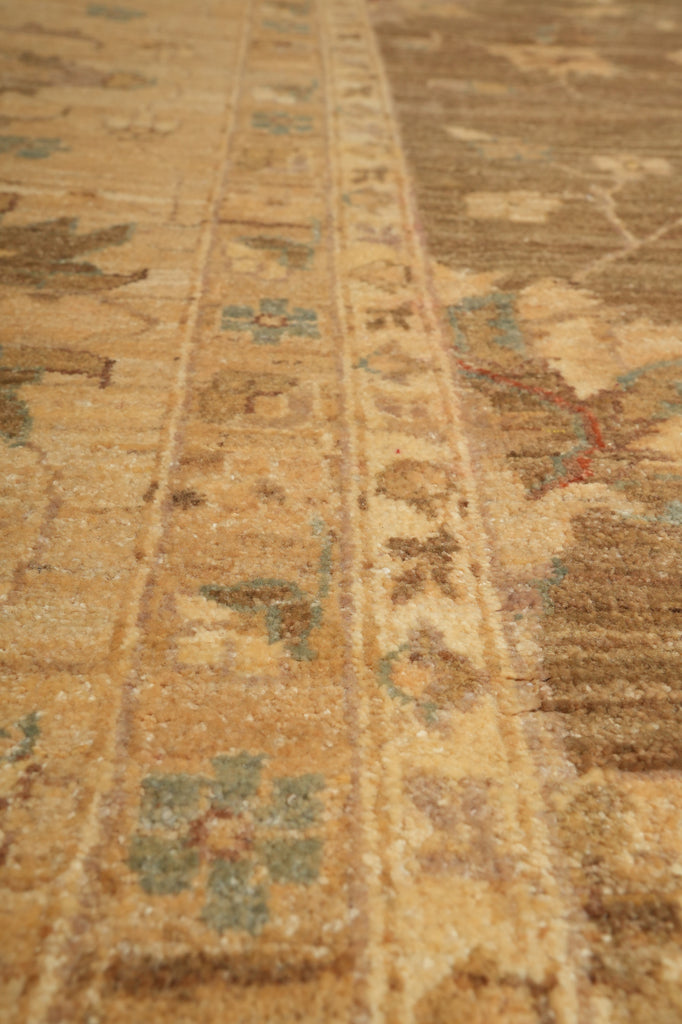 Close-up of a vintage patterned rug with a warm tan and brown base, featuring faded blue, green, and red floral motifs.