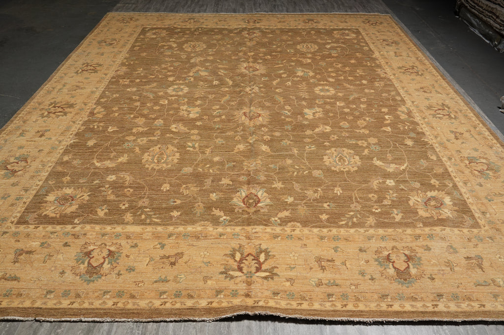 A large traditional area rug with an intricate floral and medallion pattern, shown laid out on a dark gray floor. The rug features a warm tan and beige base with muted brown, sage green, and light blue accents.
