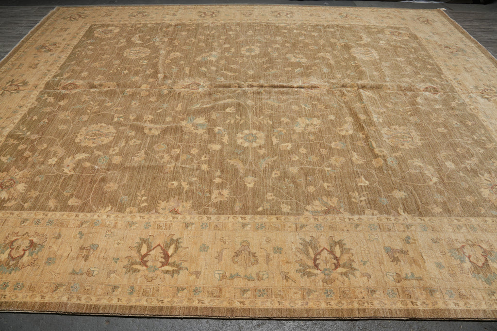 A large vintage-style area rug with an intricate floral and geometric pattern, featuring a warm tan and beige base with muted brown and light blue accents, laid out on a dark floor.
