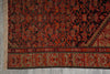 Load image into Gallery viewer, A close-up of a patterned rug showing a dark red and black central field with a beige and red geometric border, finished with a fringed edge on the left.
