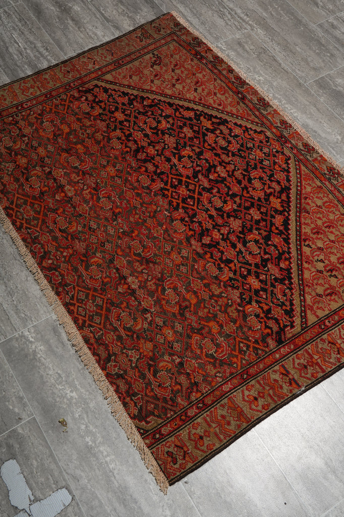A traditional oriental area rug with an intricate floral pattern in deep red, brown, and black, laid out diagonally on a gray tiled floor.