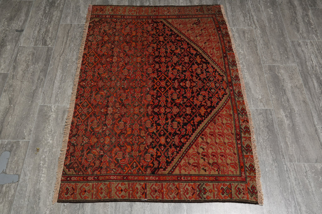 A rectangular traditional Persian-style area rug with a complex floral and geometric pattern, laid flat on a gray wood-look floor. The rug features a dominant rust-red and dark brown field with a large dark central diamond panel and a patterned border.