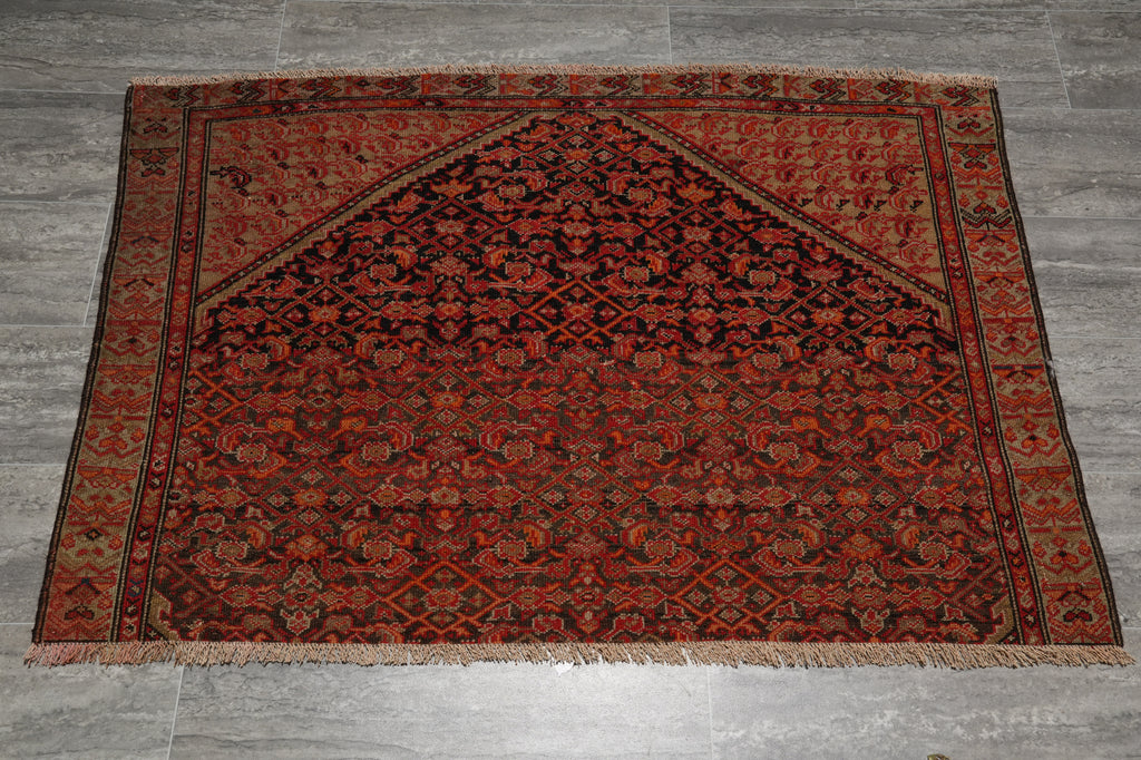A traditional Persian-style area rug with a dark red and black central field, floral motifs, and a patterned border, laid flat on a gray tiled floor.