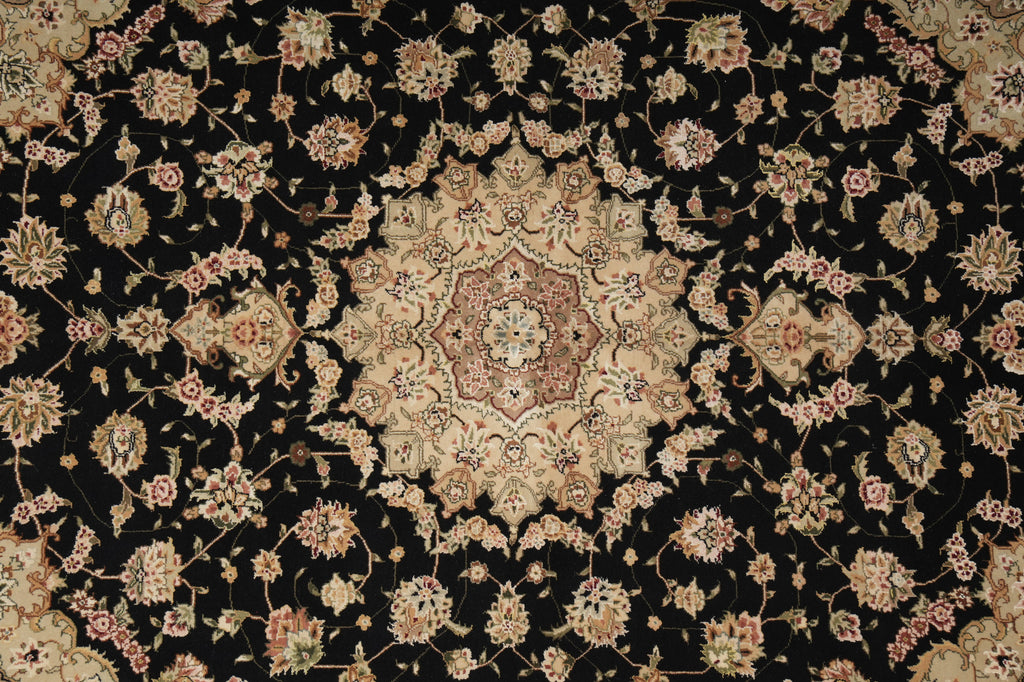 An ornate traditional Persian-style rug with a black background and a large central floral medallion, surrounded by intricate floral motifs in beige, pink, and muted blue.