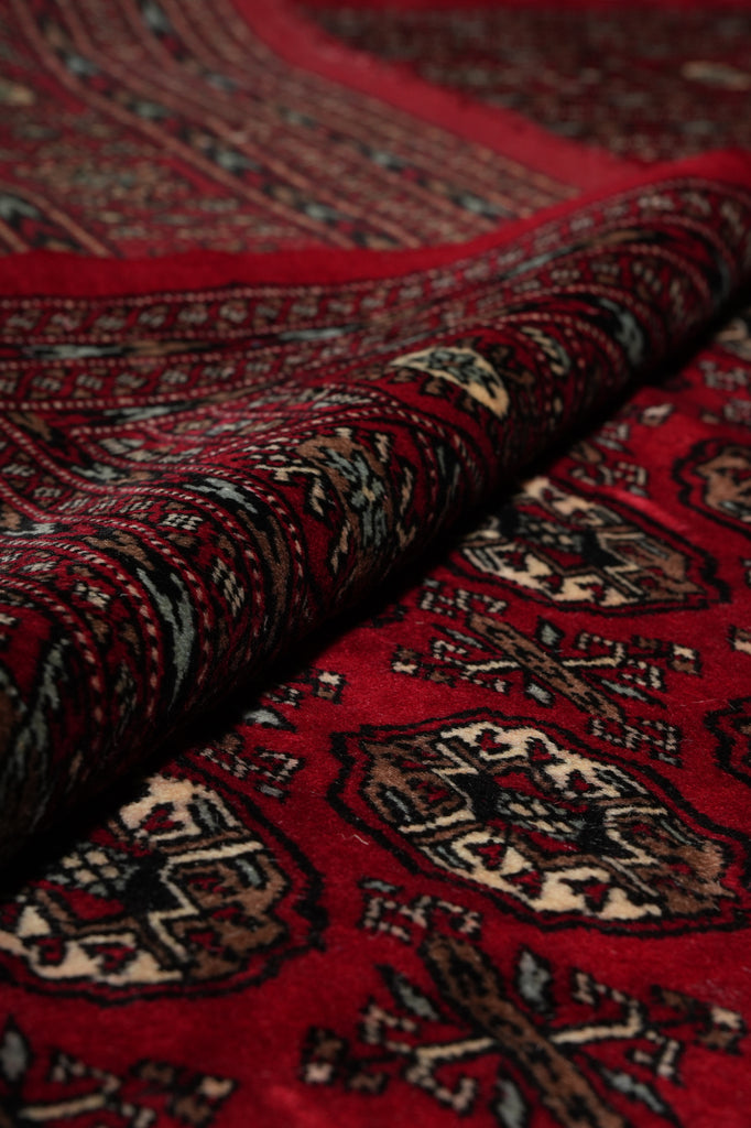 A close-up of a folded red patterned rug or textile with intricate geometric and floral motifs in dark brown, beige, and black.