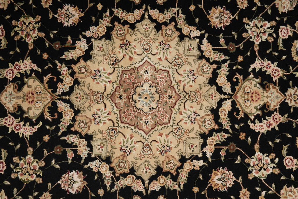 A close-up of an ornate traditional patterned rug with a black background and beige, pink, and green floral medallion motifs.