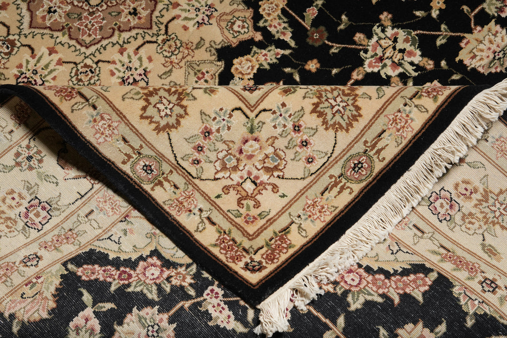A close-up of a traditional oriental rug with a cream and black floral pattern, featuring a V-shaped corner with fringe trim.