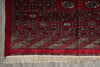 Load image into Gallery viewer, A close-up of a traditional patterned rug corner with a deep red field, geometric borders, and cream fringe along the bottom edge.
